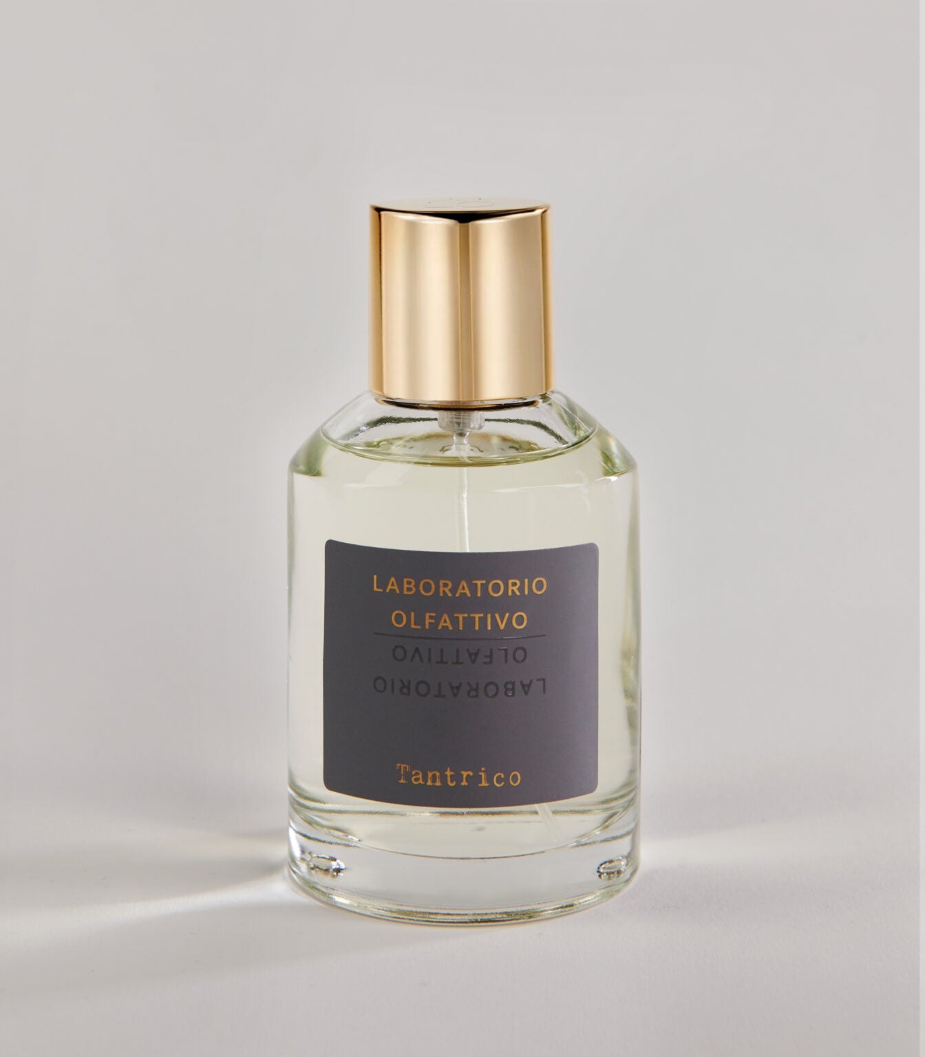 A clear glass Tantrico - Laboratorio Olfattivo TESTER perfume bottle with a gold cap, featuring gold text on a gray label, is set against a plain light background.