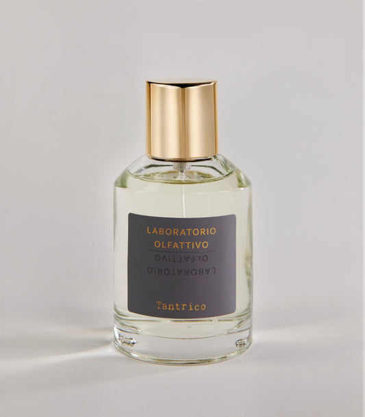 A clear glass Tantrico - Laboratorio Olfattivo TESTER perfume bottle with a gold cap, featuring gold text on a gray label, is set against a plain light background.