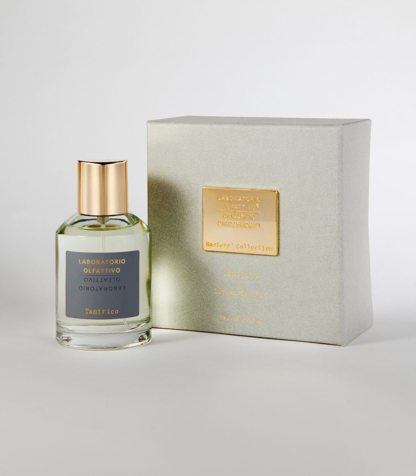 A bottle of Tantrico by Laboratorio Olfattivo, featuring a gold cap, stands beside its matching silver-grey box with a gold label and embossed text. Both are showcased against a plain white background.