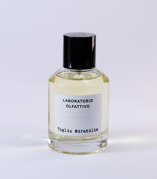 A clear glass bottle of Tiglio Mirabilis Eau de Parfum by Laboratorio Olfattivo, accented with a black cap and label, evokes floral and spicy notes and is photographed against a plain white background.