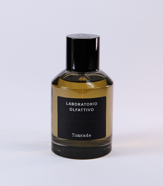 A bottle of Tonkade Eau de Parfum by Laboratorio Olfattivo features a black cap and label, golden liquid, and rich Tonka Bean notes, set against a plain light background.