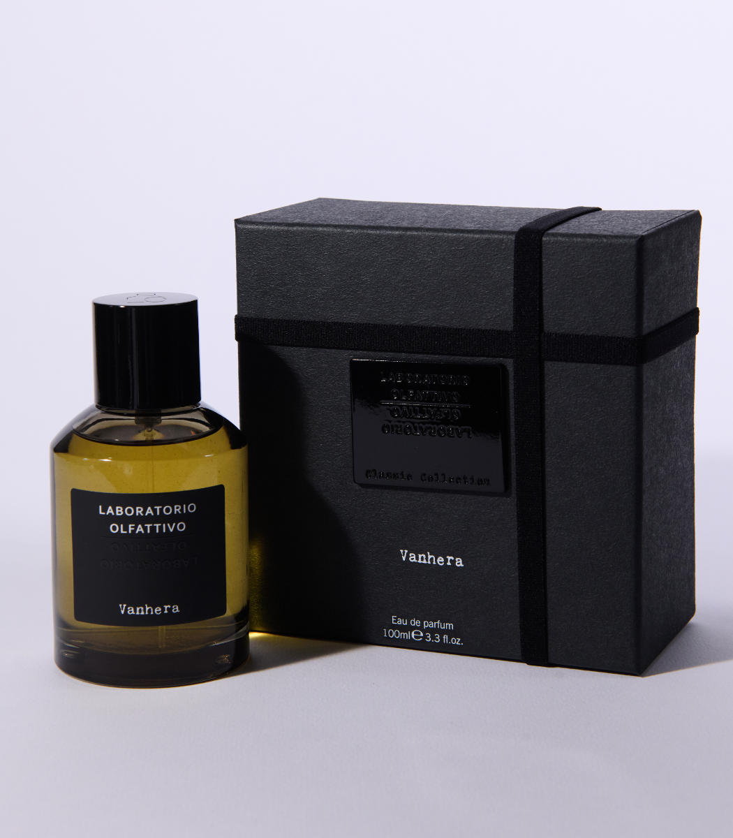 A clear bottle of Vanhera - Laboratorio Olfattivo perfume stands beside its sleek black box, both featuring minimalist black labels with white text, set against a plain light background to showcase this signature scent by Laboratorio Olfattivo.
