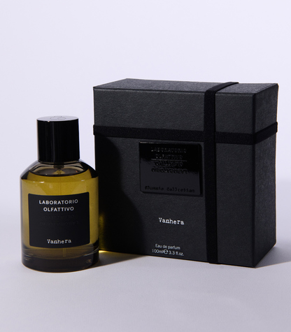 A clear bottle of Vanhera - Laboratorio Olfattivo perfume stands beside its sleek black box, both featuring minimalist black labels with white text, set against a plain light background to showcase this signature scent by Laboratorio Olfattivo.