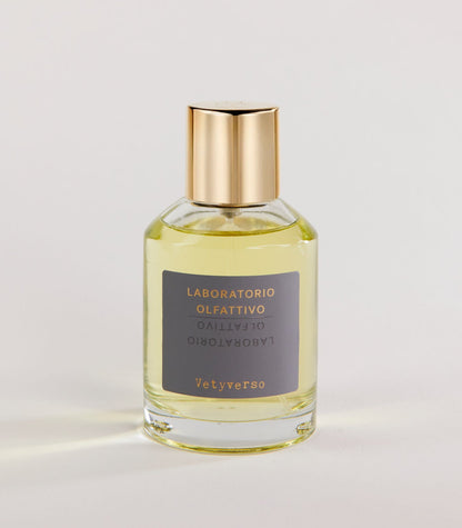 A clear glass bottle of Laboratorio Olfattivo Vetyverso TESTER perfume with a gold cap contains light yellow liquid. The label features gold and white text on gray. The bottle rests on a plain, light surface.