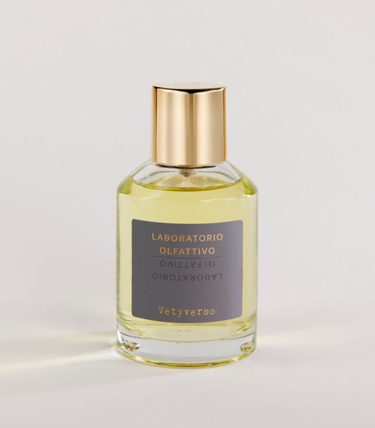 A clear glass bottle of Laboratorio Olfattivo Vetyverso TESTER perfume with a gold cap contains light yellow liquid. The label features gold and white text on gray. The bottle rests on a plain, light surface.